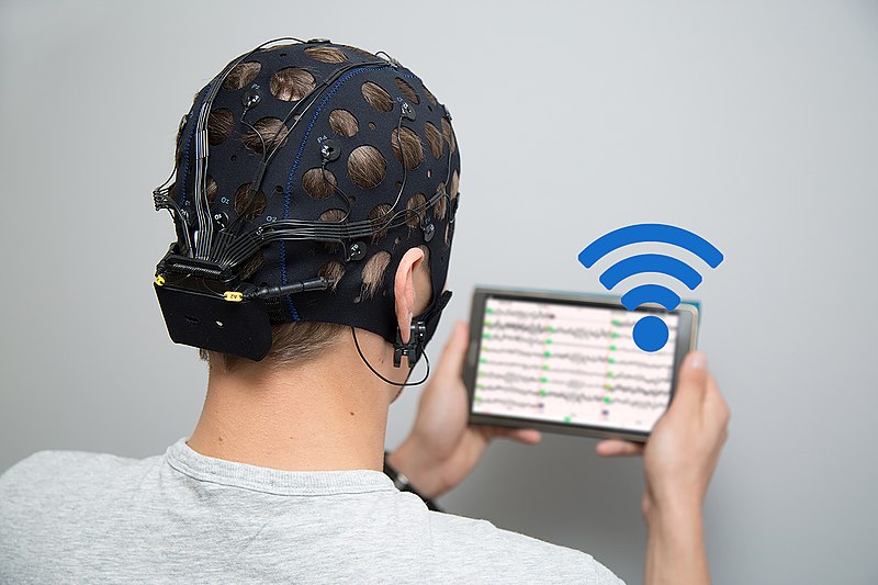 Image of someone holding a device while wearing an EEG cap